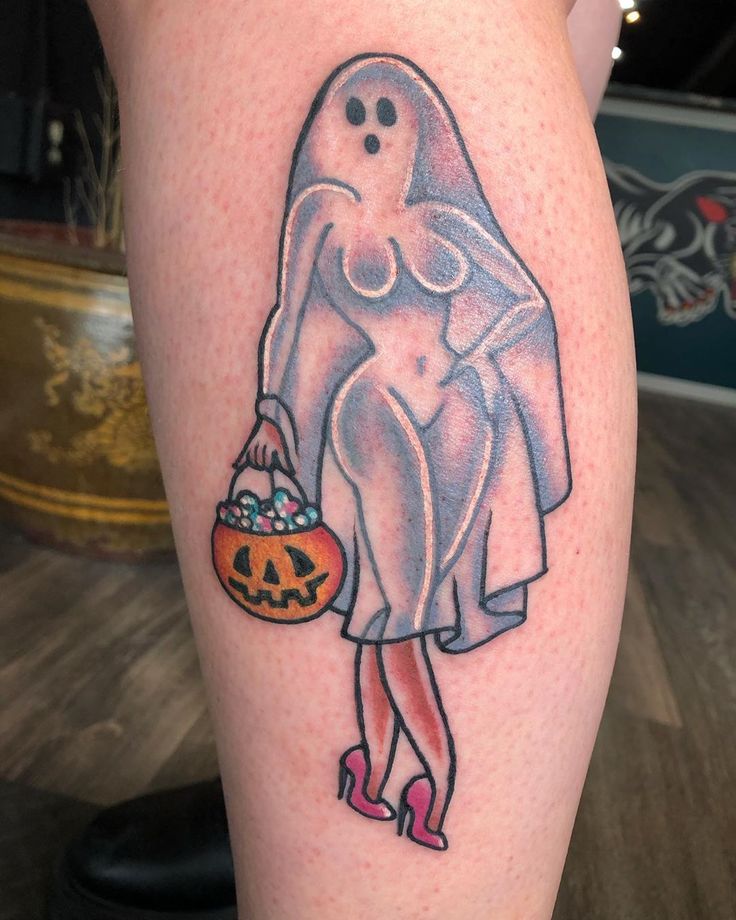 a woman with a ghost tattoo on her leg holding a pumpkin and tricking jack - o - lantern