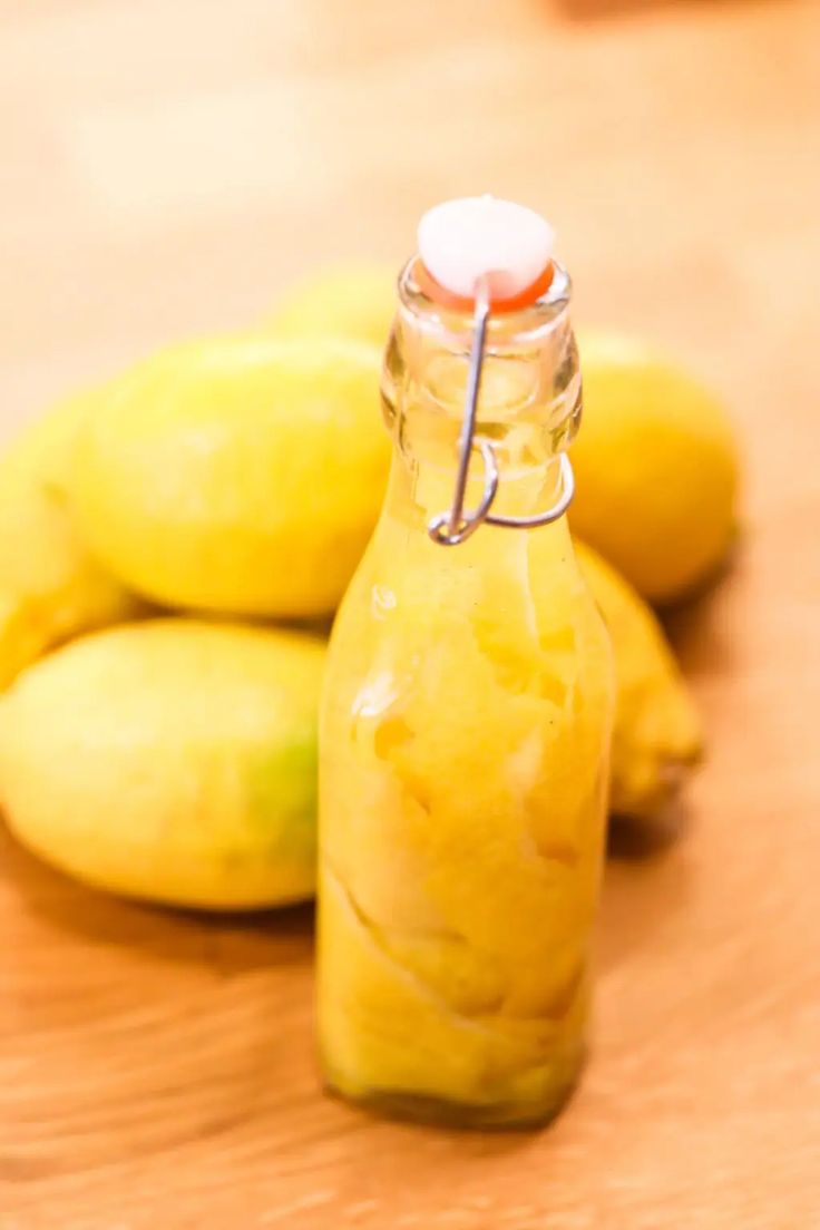 a glass bottle filled with yellow liquid sitting on top of a wooden table next to bananas