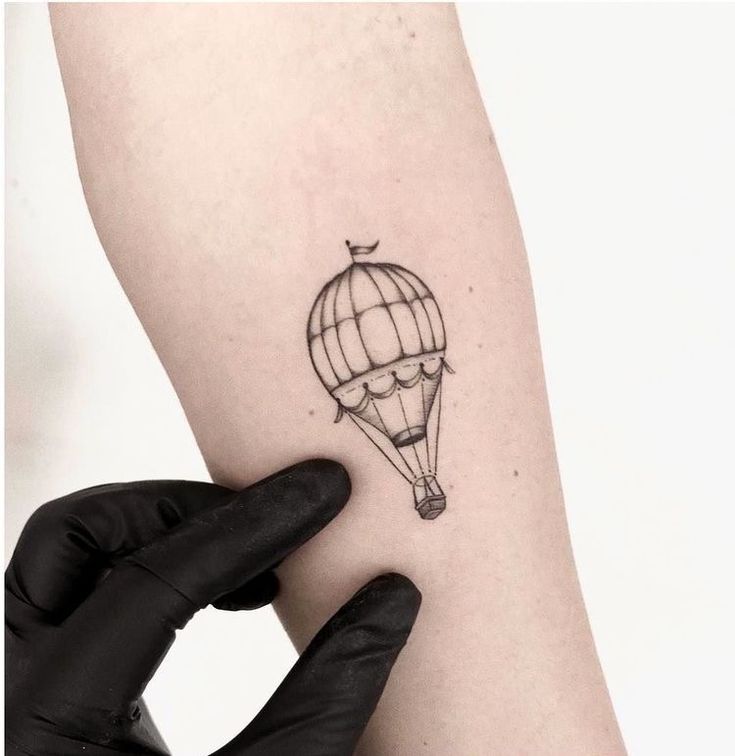 a small hot air balloon tattoo on the left inner arm and wrist, with an arrow pointing up at it