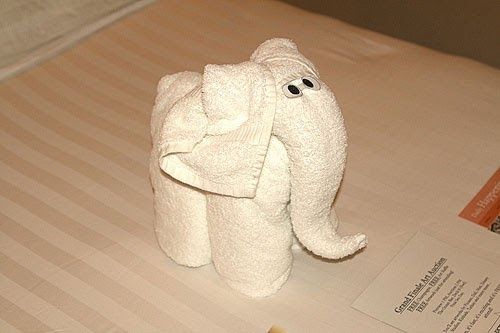 an elephant made out of toilet paper sitting on top of a bed next to a book