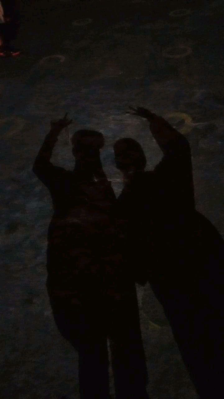 two people standing next to each other with their hands up in the air at night