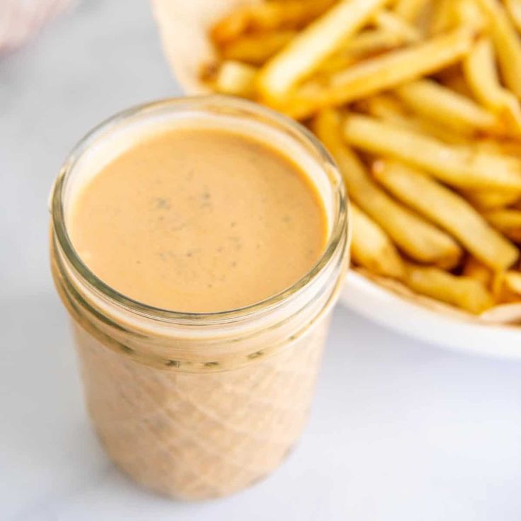 a glass jar filled with sauce next to a plate of fries