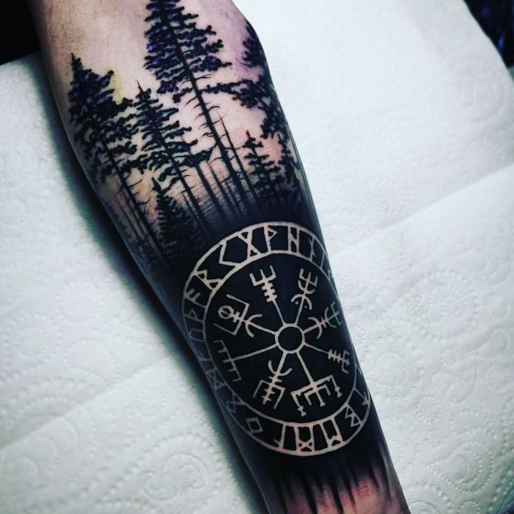 a man's arm with a compass and trees on it