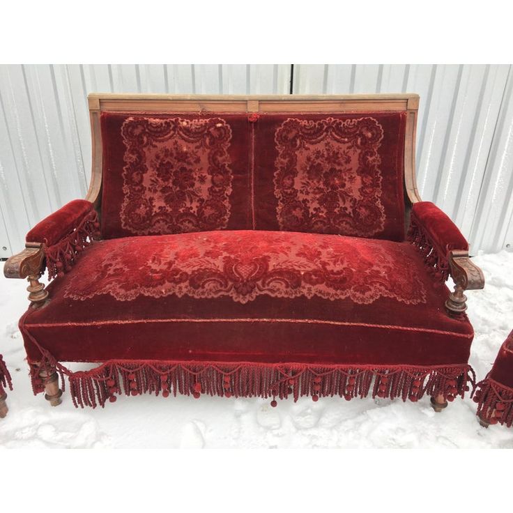 a red velvet couch with tassels on the legs and back, in front of a white wall