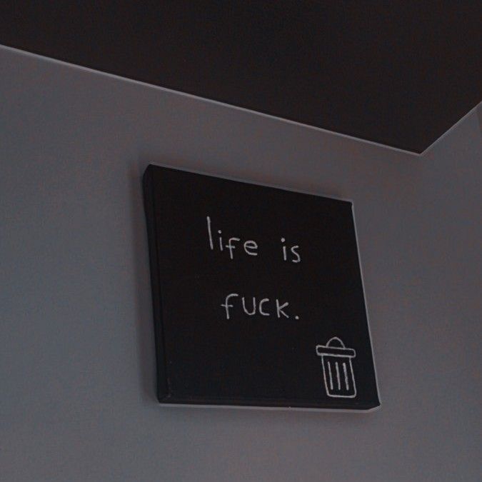 a black sign that says life is fock on the wall next to a trash can