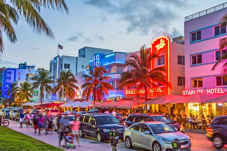 a busy street with cars and people walking on the sidewalk in front of colorful buildings