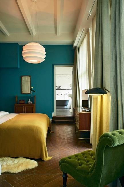 a bed room with a neatly made bed next to a green chair and a window