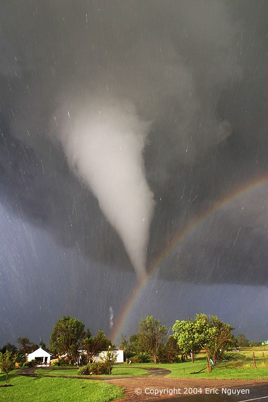 a rainbow is seen in the sky above a storm cloud and green grass with houses on either side