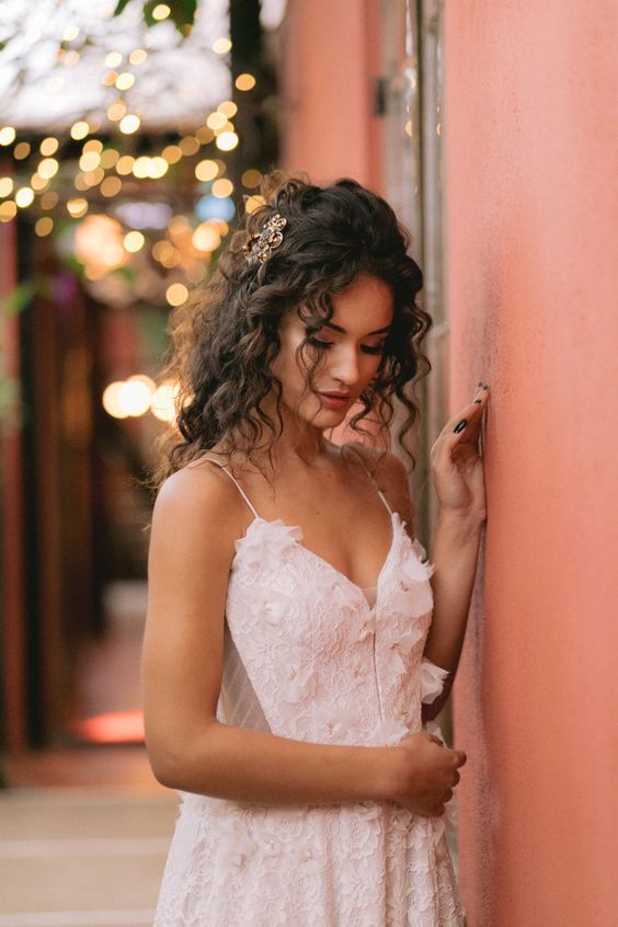 a woman in a white dress leaning against a pink wall and looking at her cell phone