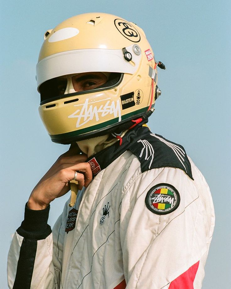 a man wearing a helmet and jacket with his hand to his mouth while standing in front of a blue sky