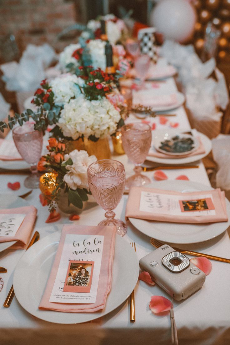 the table is set with pink and white plates, napkins, silverware, and flowers