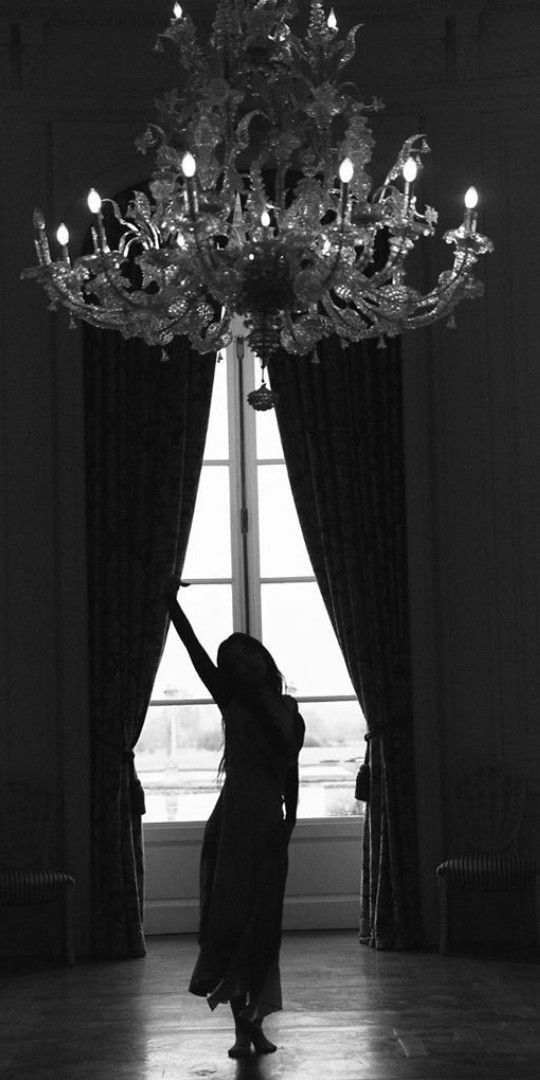 a woman standing in front of a chandelier with her hand up to the ceiling