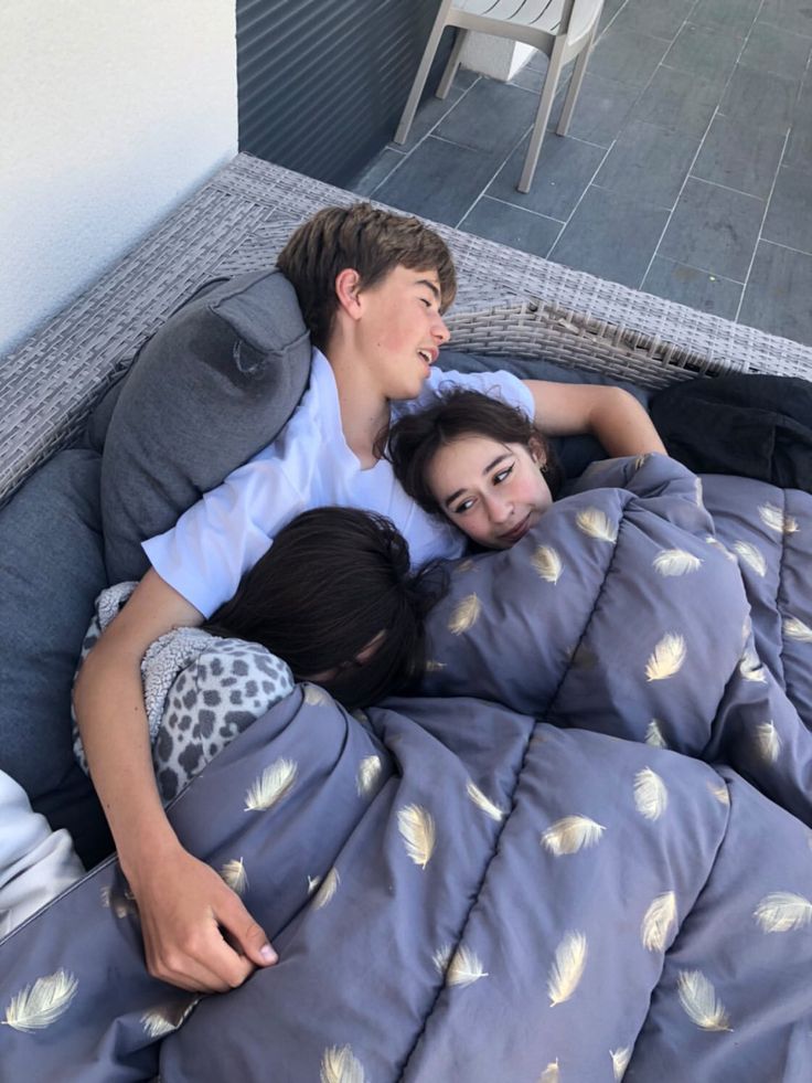 two young people laying in bed together with pillows on top of each other and smiling