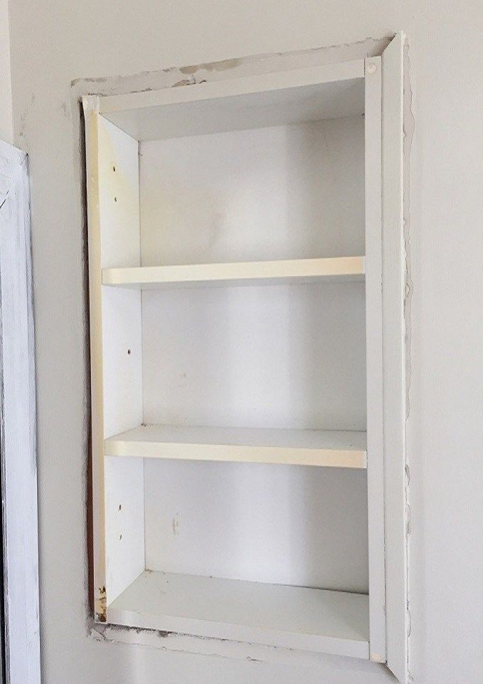 an empty shelf in the corner of a room with white paint and peeling paint on it