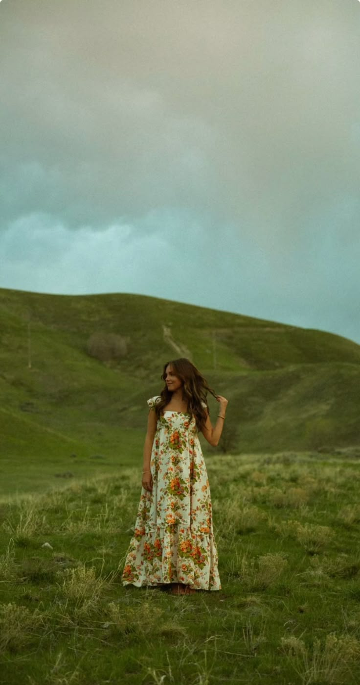 a woman standing in a field with her hair blowing in the wind, wearing a floral dress