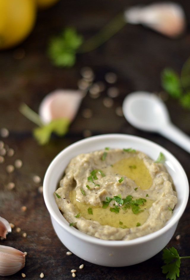 a white bowl filled with hummus on top of a table next to garlic and lemon wedges