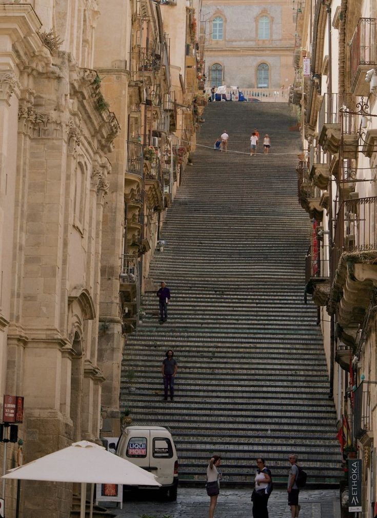 some people are standing on the stairs in an old city with stone buildings and white umbrellas