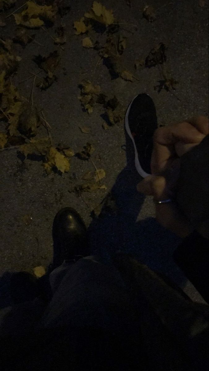 the person is holding their shoes while sitting on the ground with leaves all around them