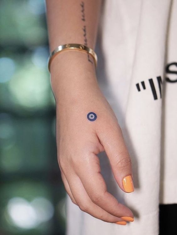 a woman's hand with an evil eye tattoo on her left wrist and yellow nail polish