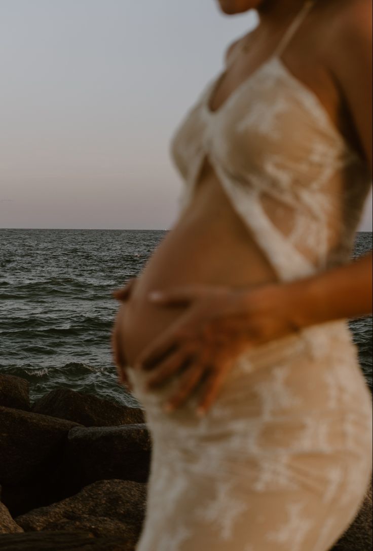 a pregnant woman standing in front of the ocean