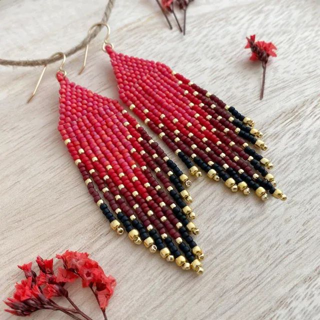 red, black and gold beaded earrings on a white table next to dried flowers