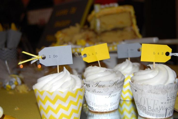 three cupcakes with white frosting and yellow tags on them sitting on a table