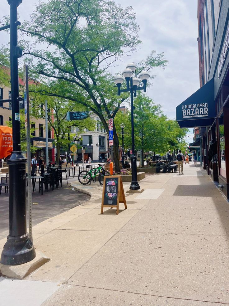 an empty sidewalk in the middle of a city with tables and chairs on each side