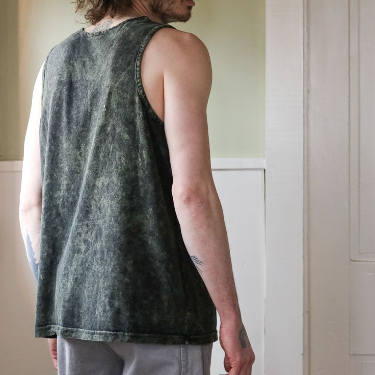 a man with long hair wearing a tank top looking at something in the distance while standing next to a door