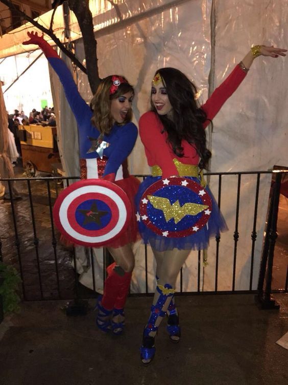 two women dressed up as superheros standing next to each other in front of a fence