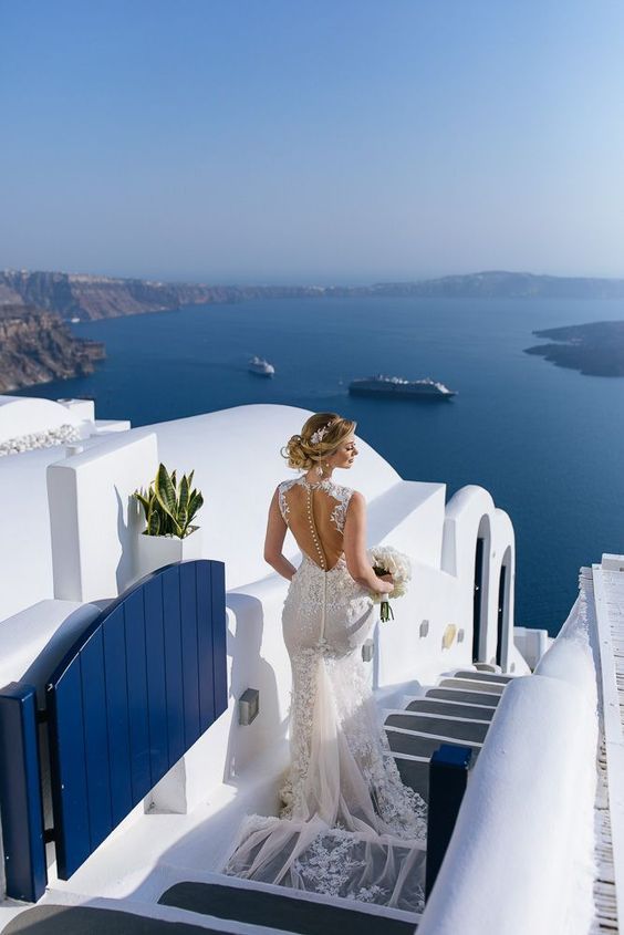 a woman in a wedding dress is standing on the stairs overlooking the water and cliffs