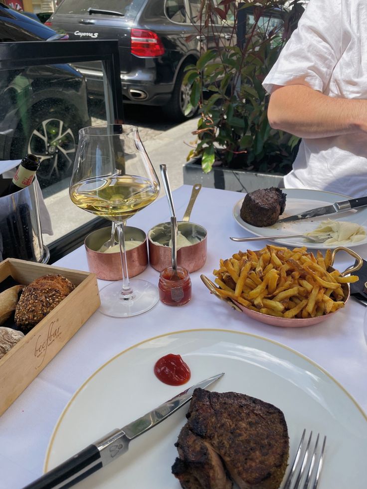 a plate with steak, french fries and some wine on the table next to it