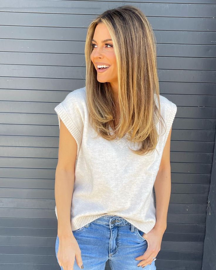 a woman standing in front of a garage door wearing blue jeans and a white sweater