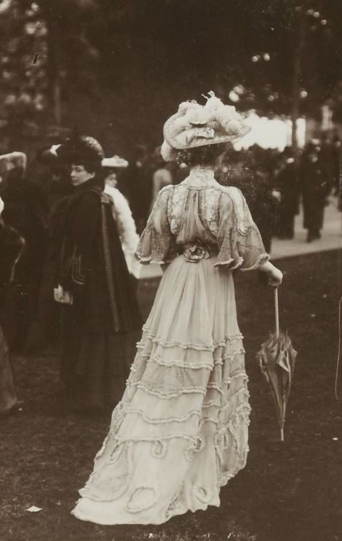 an old black and white photo of a woman in a long dress holding an umbrella