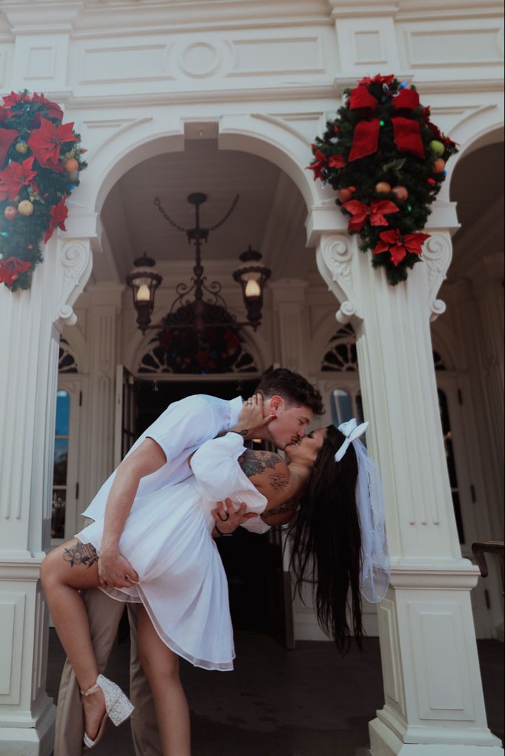 a man and woman kissing in front of a white building with wreaths on it