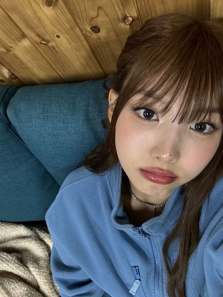 a young woman laying on top of a bed next to a wooden head board and wearing a blue jacket