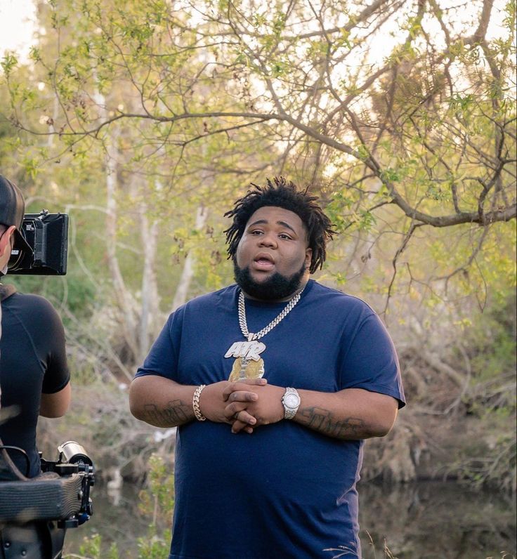 a man with dreadlocks standing in front of a camera and another person holding a cell phone