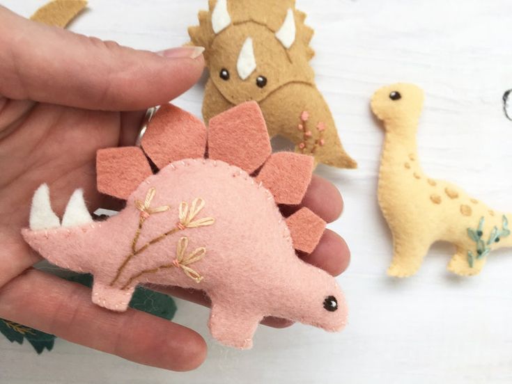 someone is holding three small dinosaur brooches in their hand, one pink and one yellow