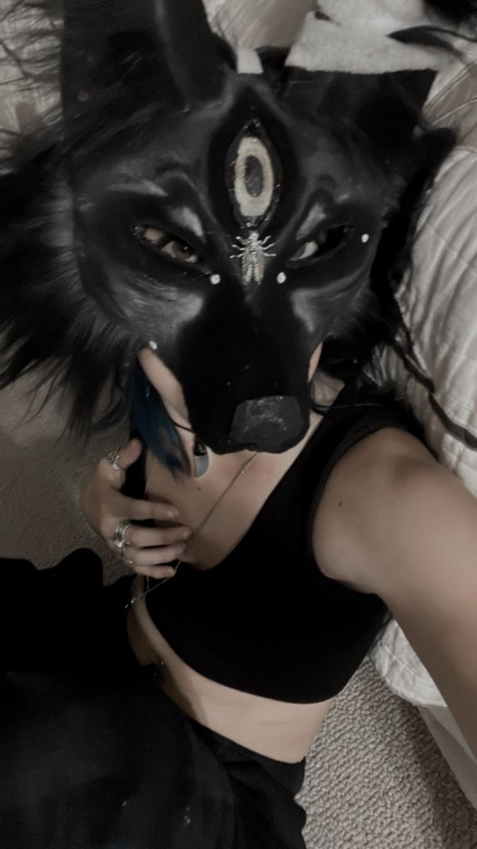 a woman wearing a black mask and holding a cell phone in her hand while laying on a bed