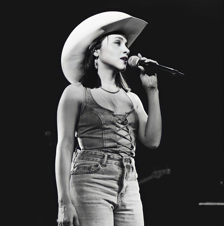 a black and white photo of a woman with a cowboy hat singing into a microphone