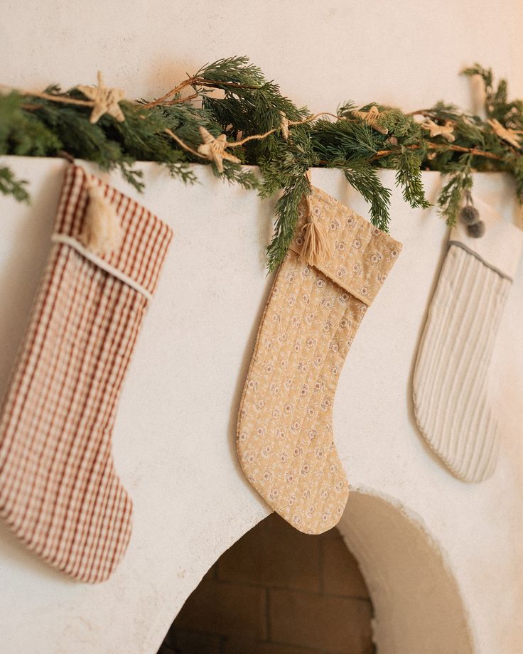 three stockings hanging on the wall next to each other with pine needles and plaid stocking