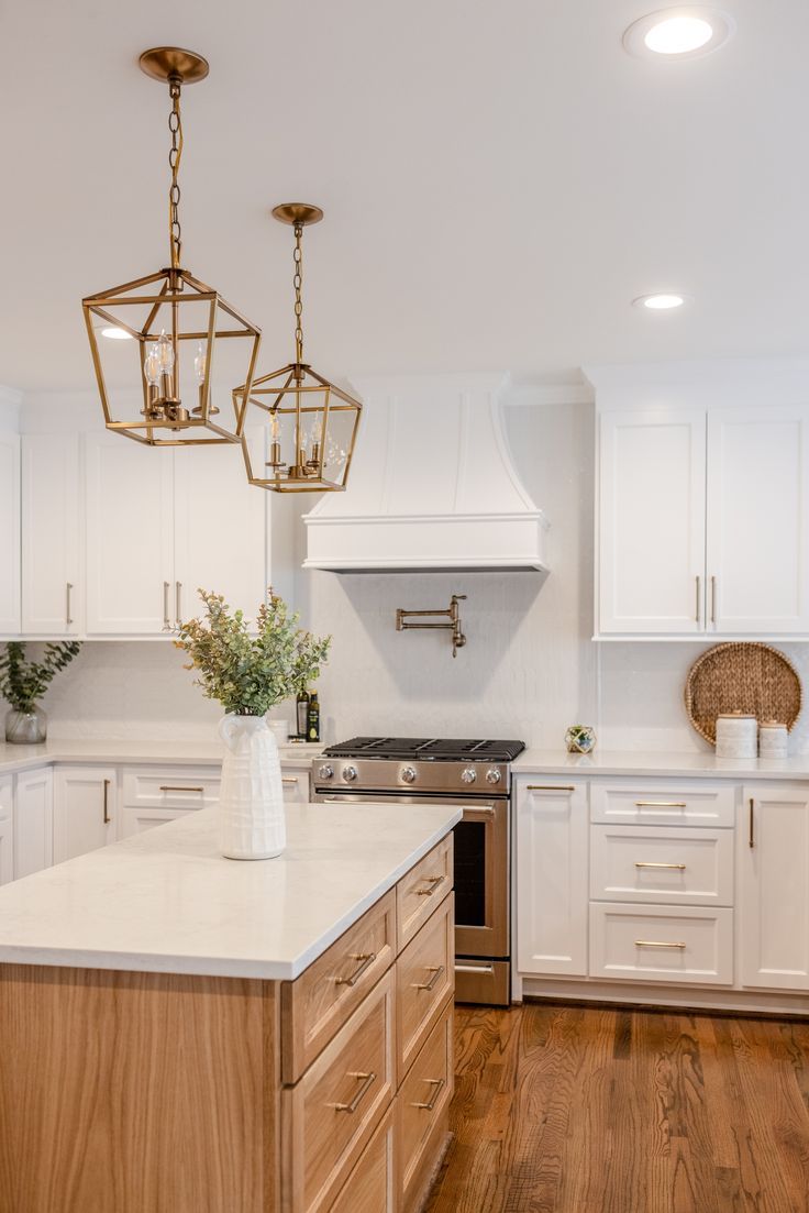 a kitchen with white cabinets and wood floors, an island in the middle is surrounded by hanging lights