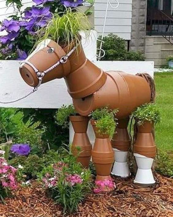 a horse made out of clay sitting in the middle of flowers and potted plants