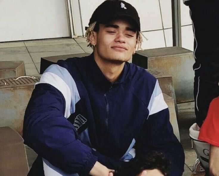 a man sitting next to another man in a baseball cap and blue jacket with his hands on his chest