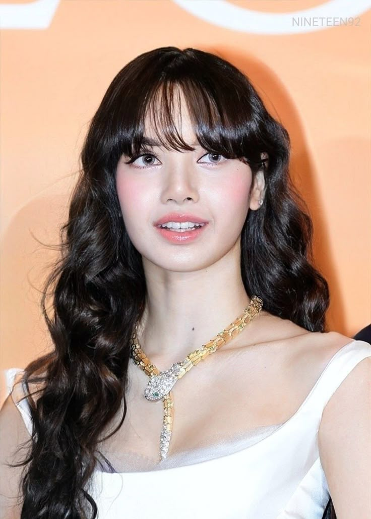 a woman with long black hair wearing a white dress and gold chain necklace on her neck