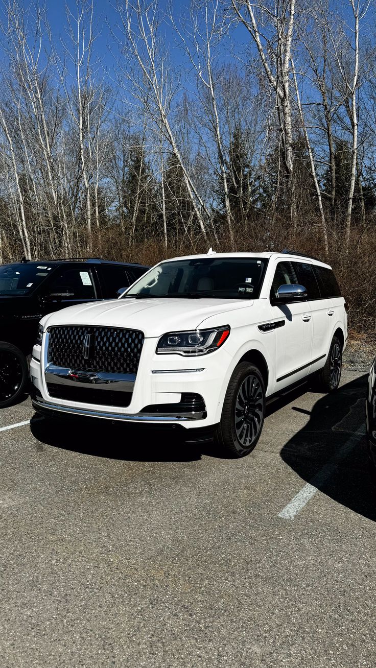 two suvs parked in a parking lot next to each other with trees in the background