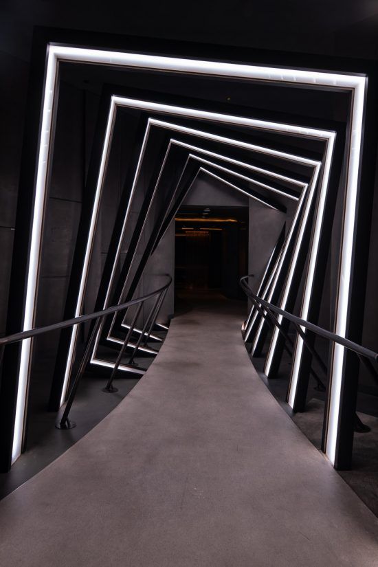 an empty tunnel with stairs and railings lit up by neon lights at the end