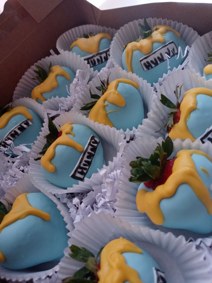 a box filled with blue and yellow cupcakes covered in frosting