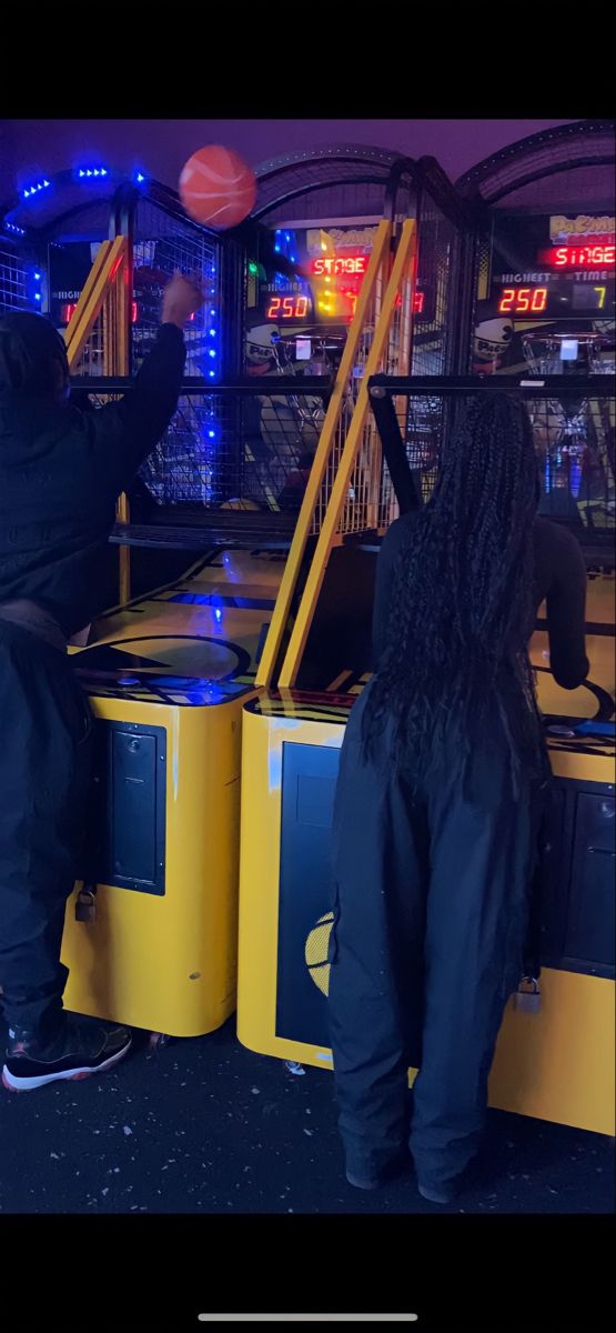 two people standing in front of an arcade machine with basketballs on it's back