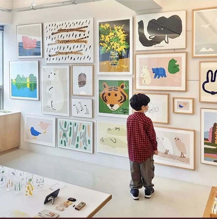 a young boy standing in front of a wall full of pictures and drawings on it