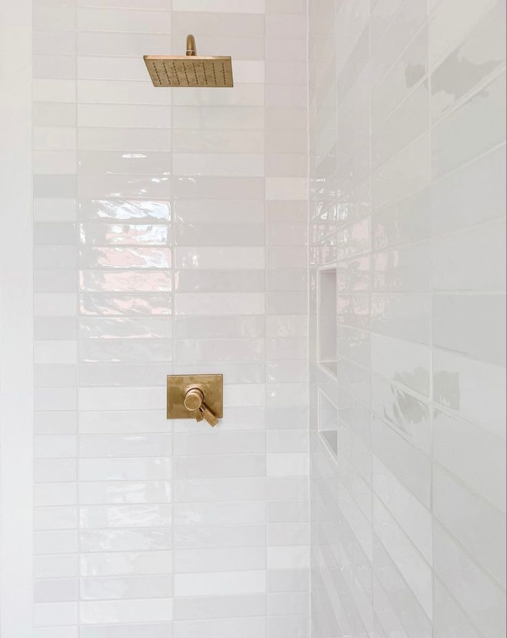 a white tiled shower with gold faucet and soap dispenser on the wall